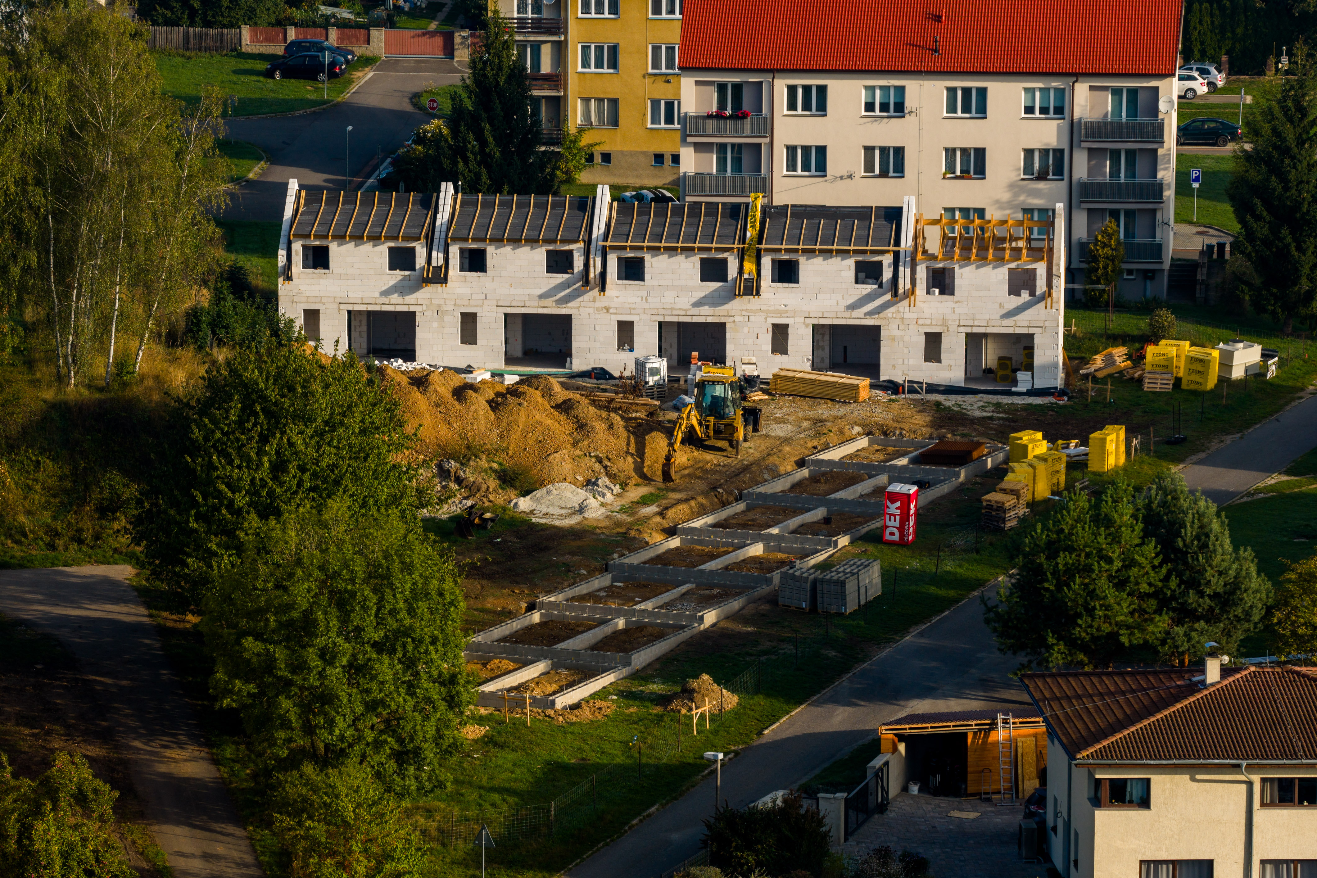 Letecký pohled: první řada domů ve hrubé stavbě s krovy, před ní základy druhé řady
